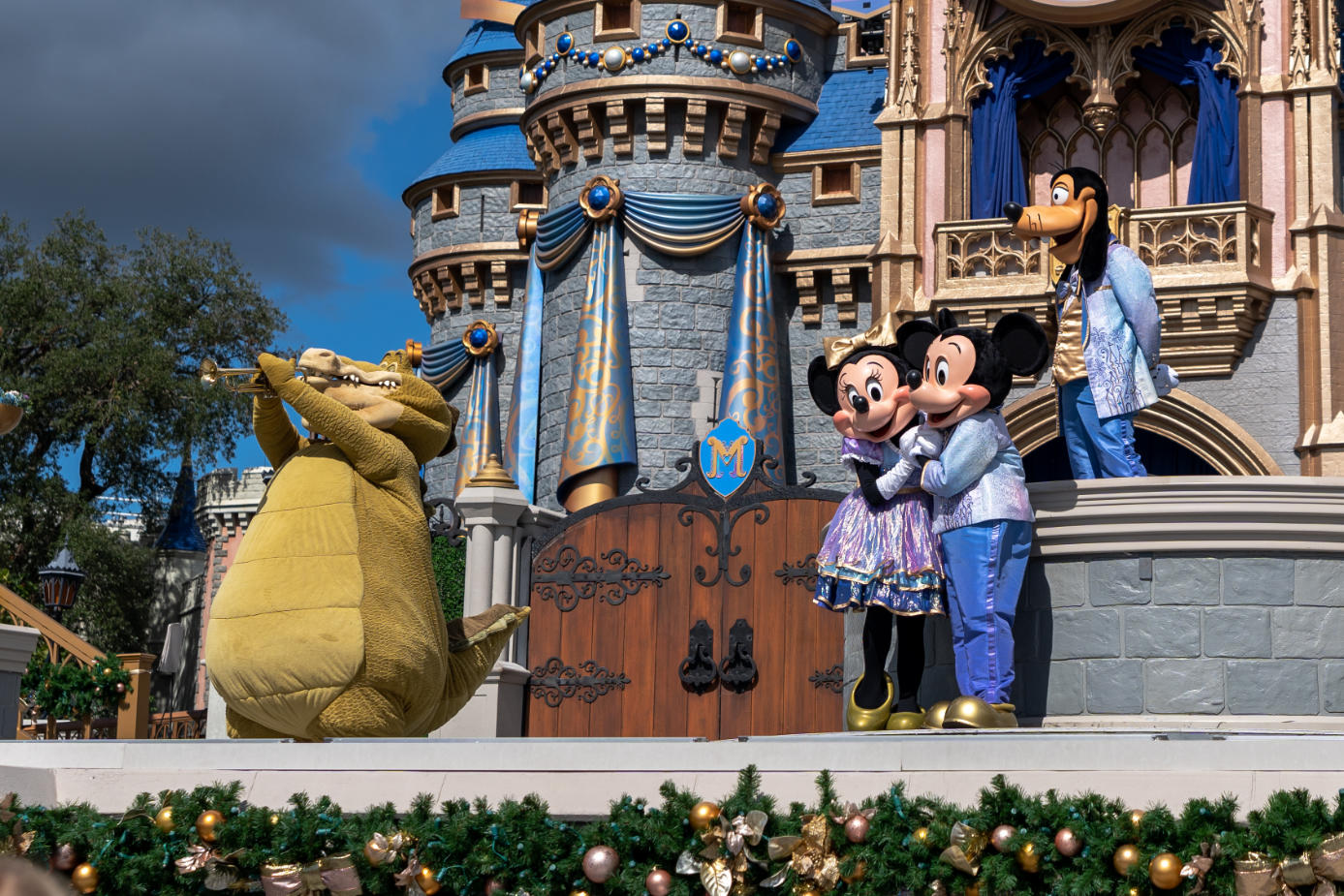 Disney characters Mickey Mouse, Minnie Mouse, Goofy, and Louis the alligator perform on stage in front of Cinderella Castle at Walt Disney World.