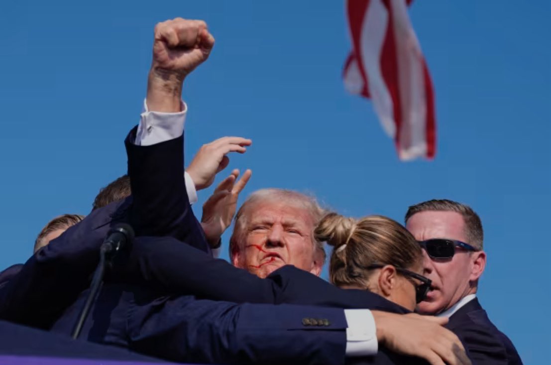 Donald Trump being escorted away after assassination attempt, blood on face
