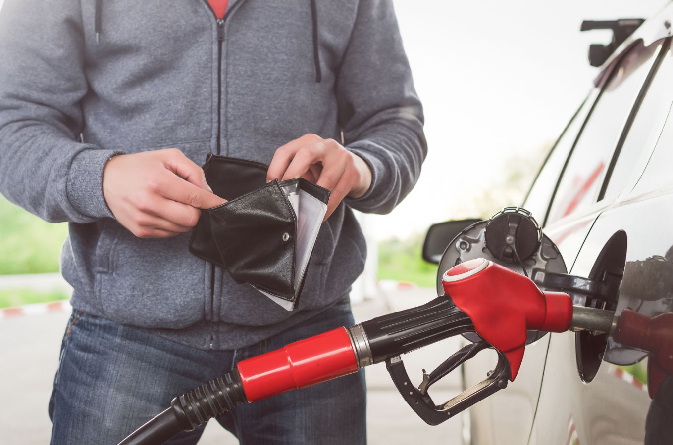 Man looks inside empty wallet while fueling car