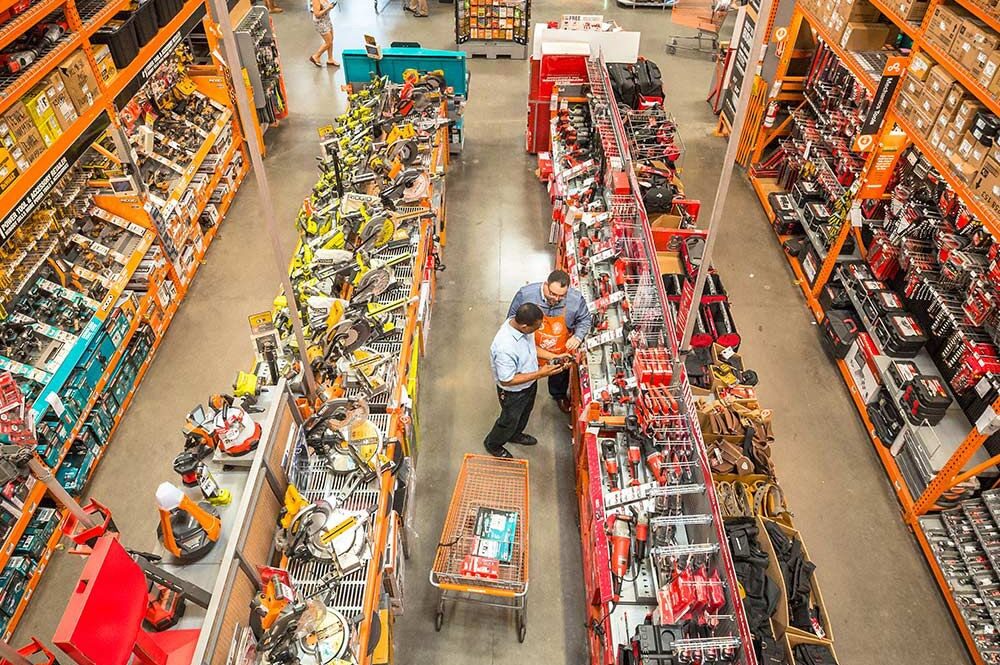 Men staring blankly at power tools inside a brightly lit Home Depot