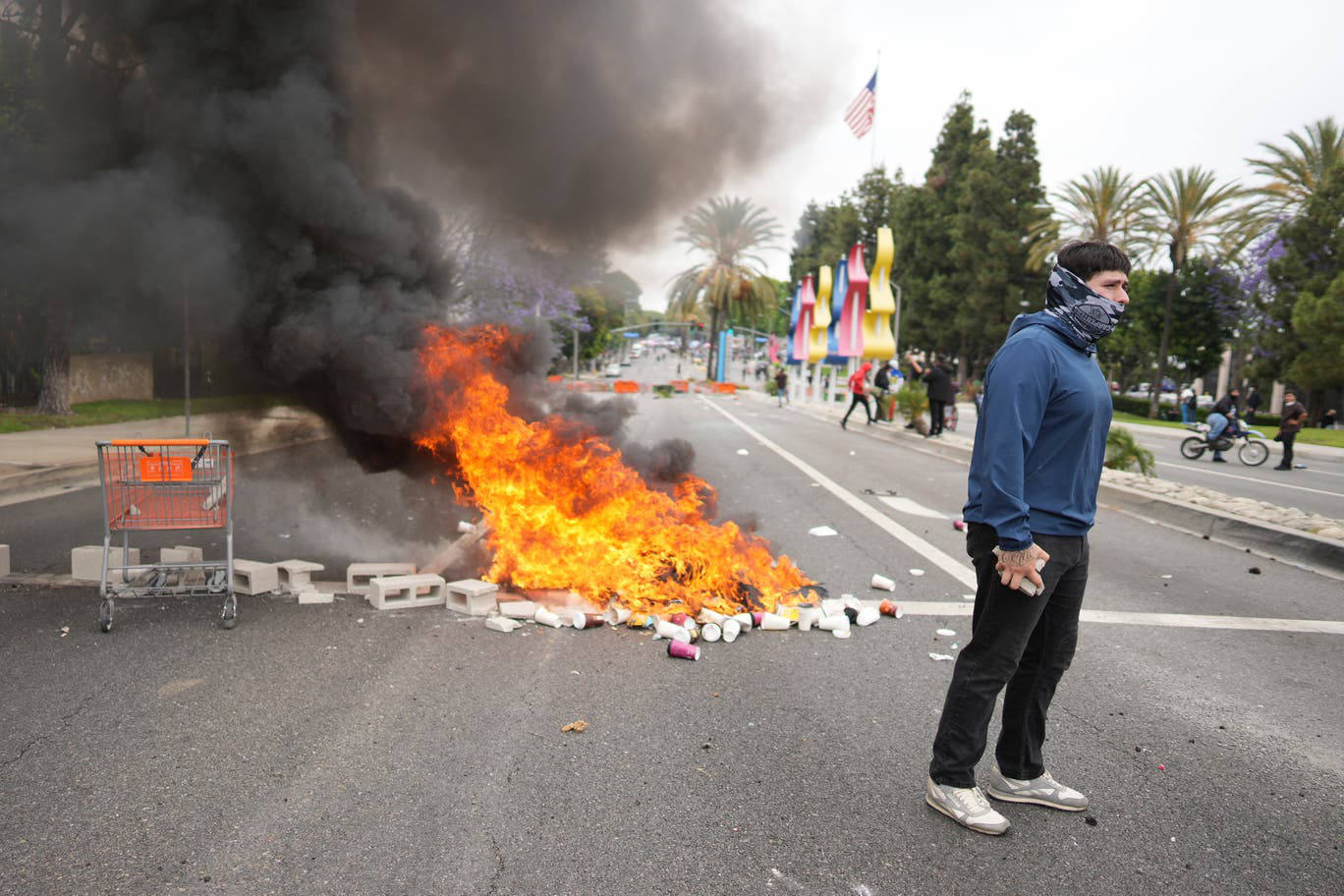 Protester stands near burning debris and smoke during street demonstration in Los Angeles