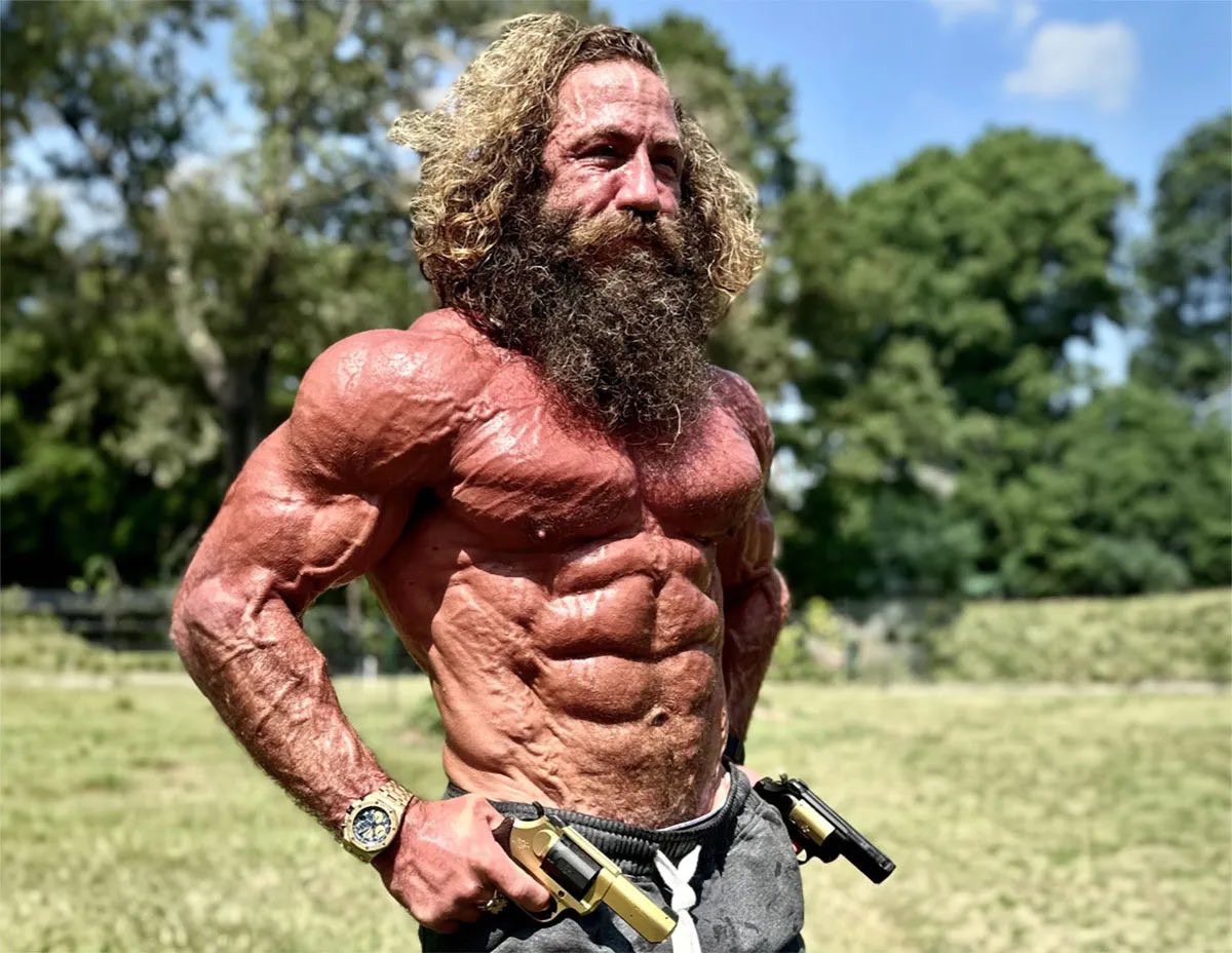 Liver King shirtless and flexing with primal intensity in a sunny field