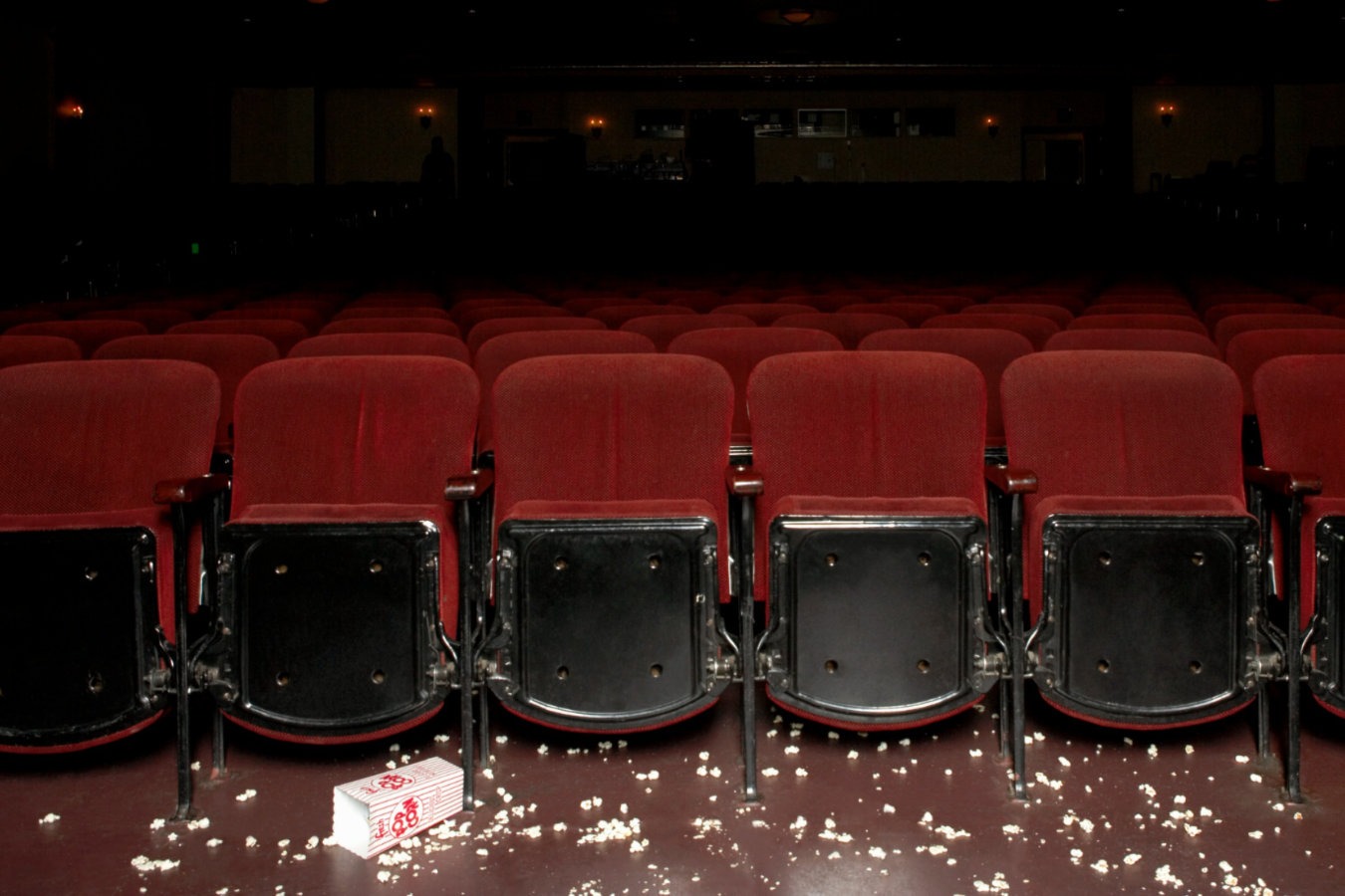 Empty theater seats with scattered popcorn and a tipped popcorn box on the floor, symbolizing a popcorn shortage.