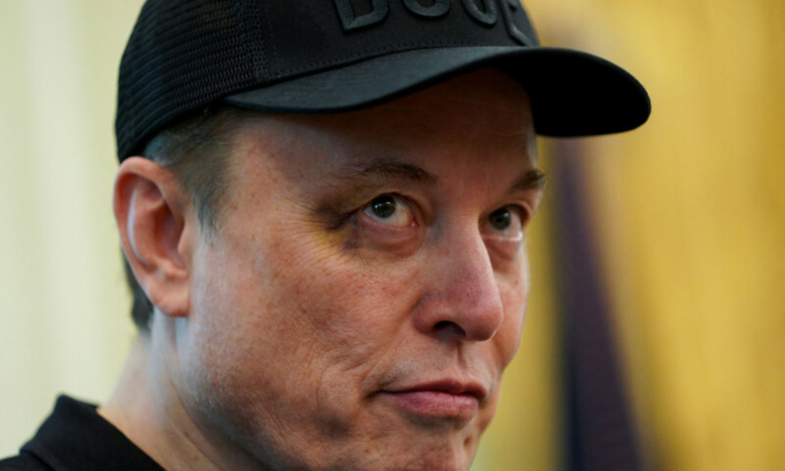 Elon Musk with a visible black eye wearing a black DOGE hat