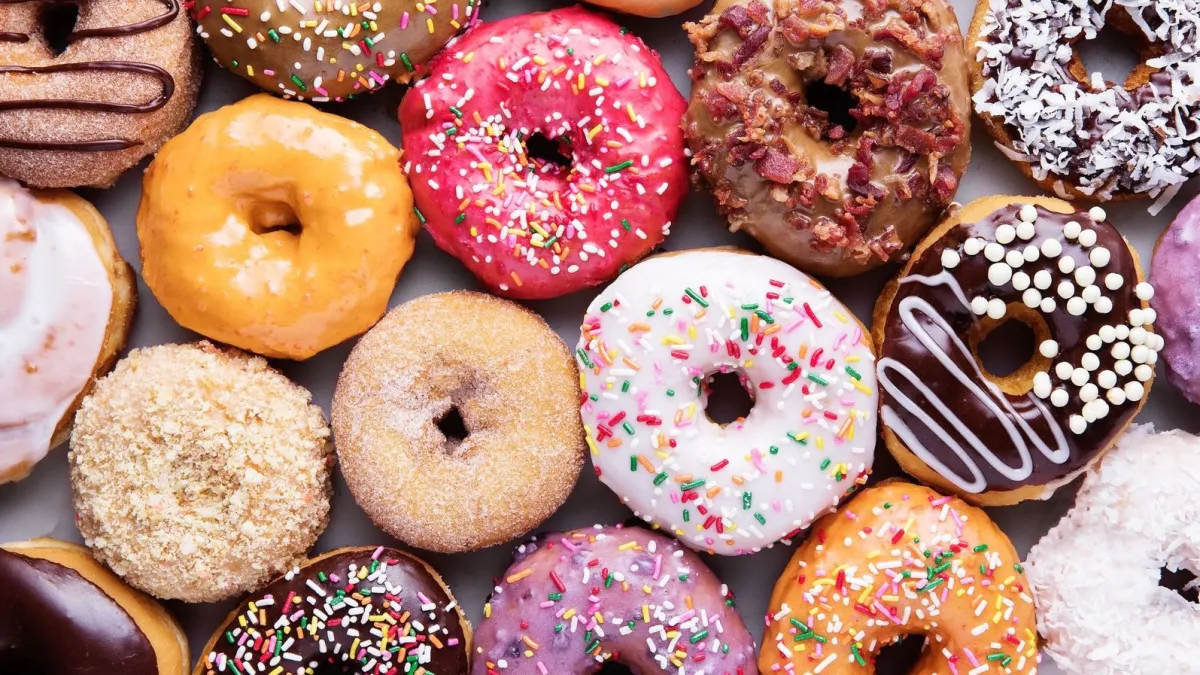 Colorful assorted donuts with frosting, sprinkles, and toppings arranged in a close-up flat lay