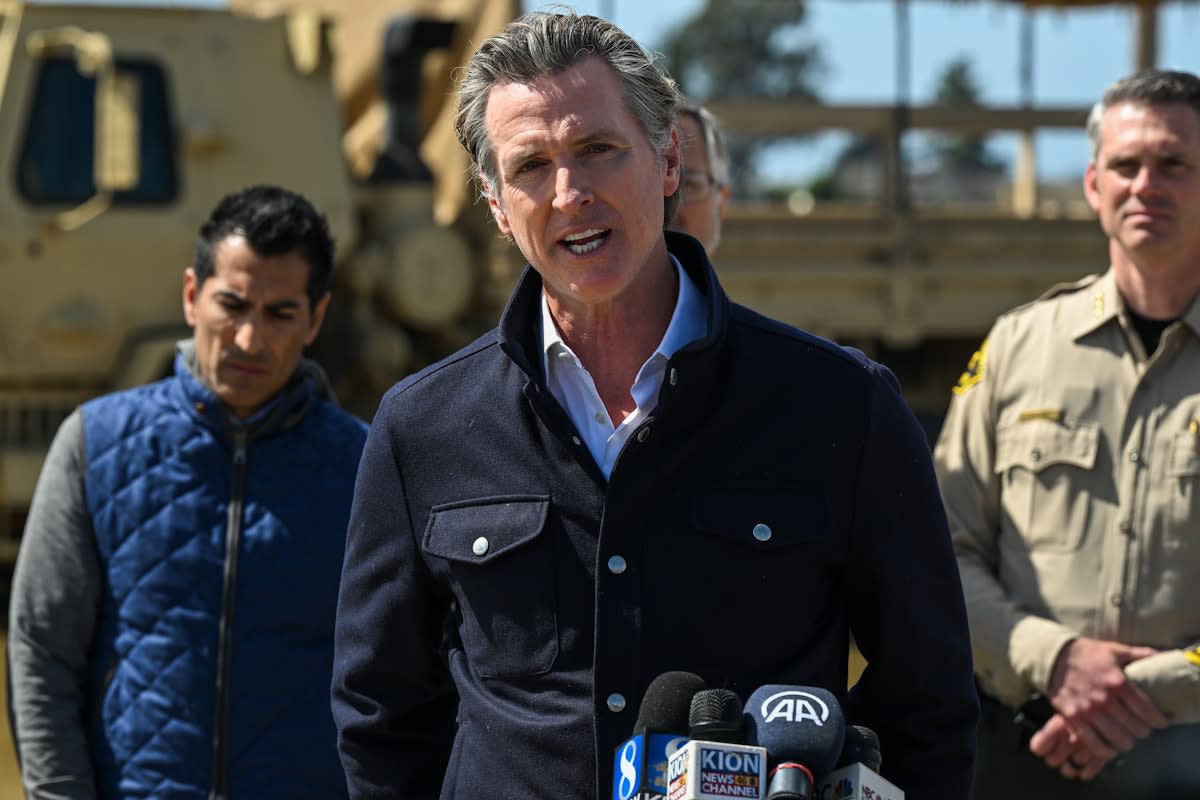 California Governor Gavin Newsom speaks at a press conference flanked by officials and National Guard vehicles during tense standoff with Trump administration