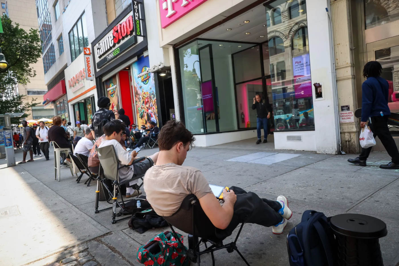 Gamers waiting in a long line outside GameStop and T-Mobile stores in lawn chairs during the Nintendo Switch 2 release.