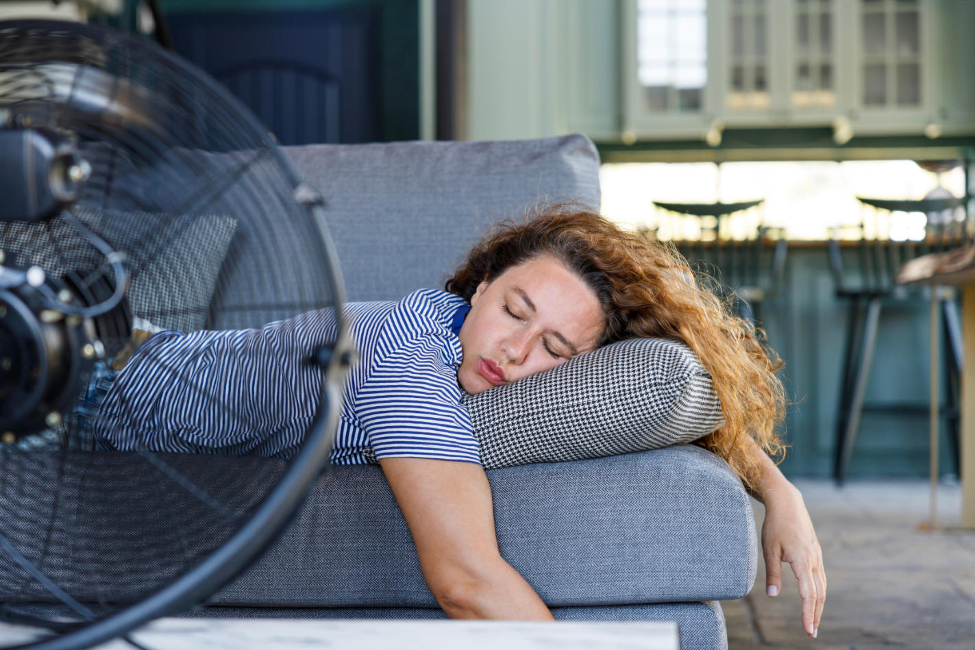 Woman passed out on couch in front of large fan during heatwave