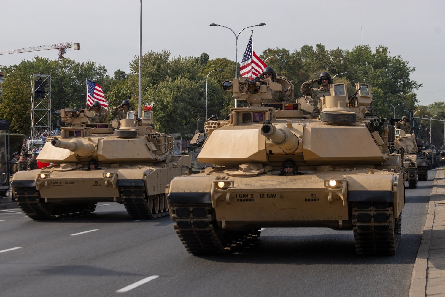 Military tanks with American flags roll down a city street as part of a parade.