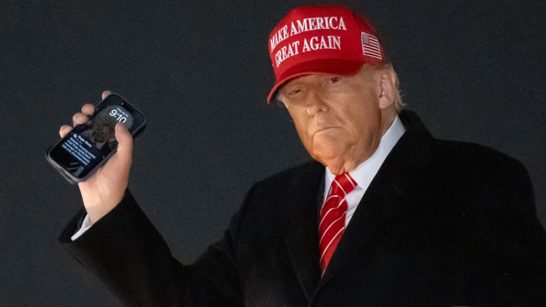 Donald Trump holding smartphone with MAGA hat while exiting Air Force One