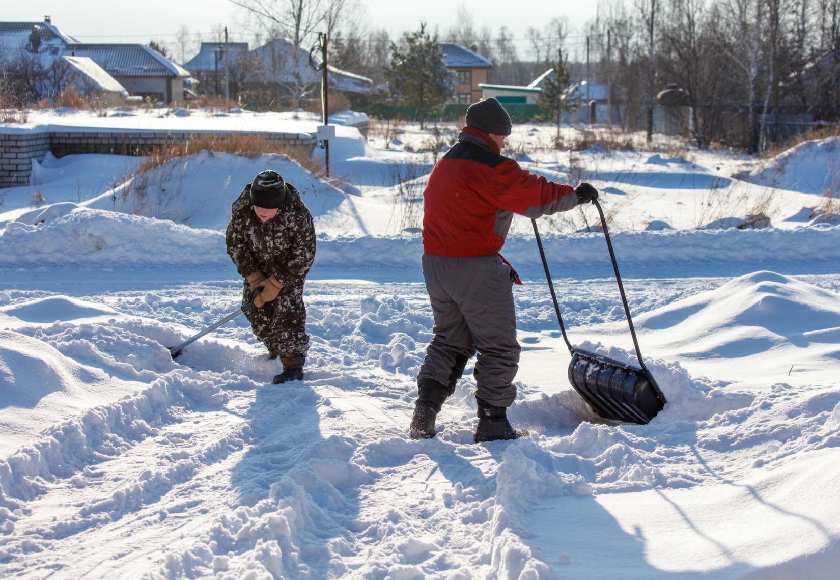 Two men are shoveling snow with a large black plastic bag
