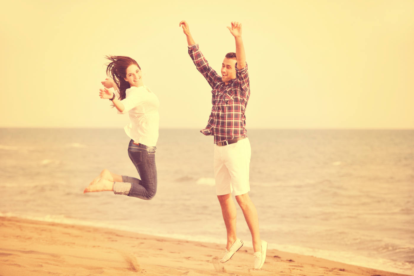 Happy couple jumping with joy on a beach, smiling and carefree under a warm golden sky