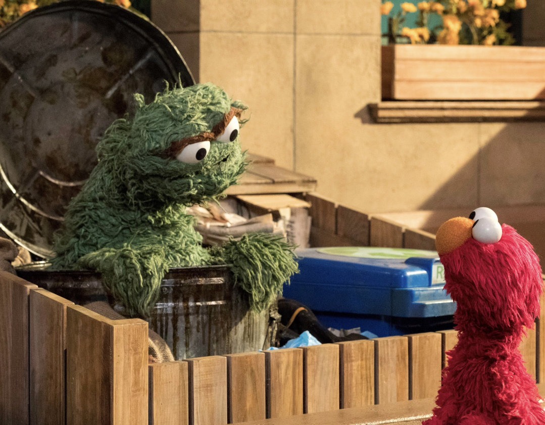 Oscar the Grouch and Elmo speaking outside a trash can