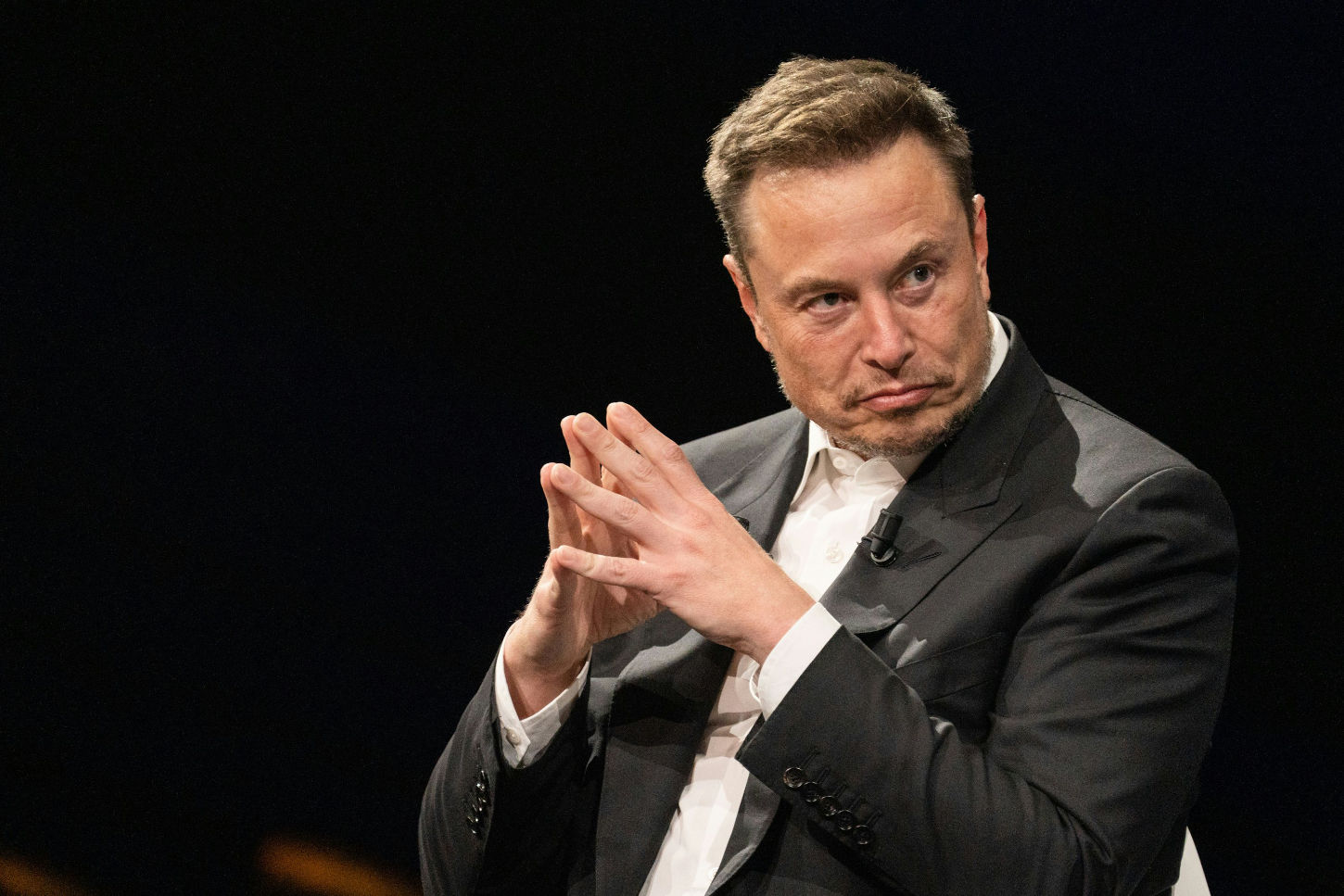 Elon Musk sitting with fingers steepled, plotting something strange