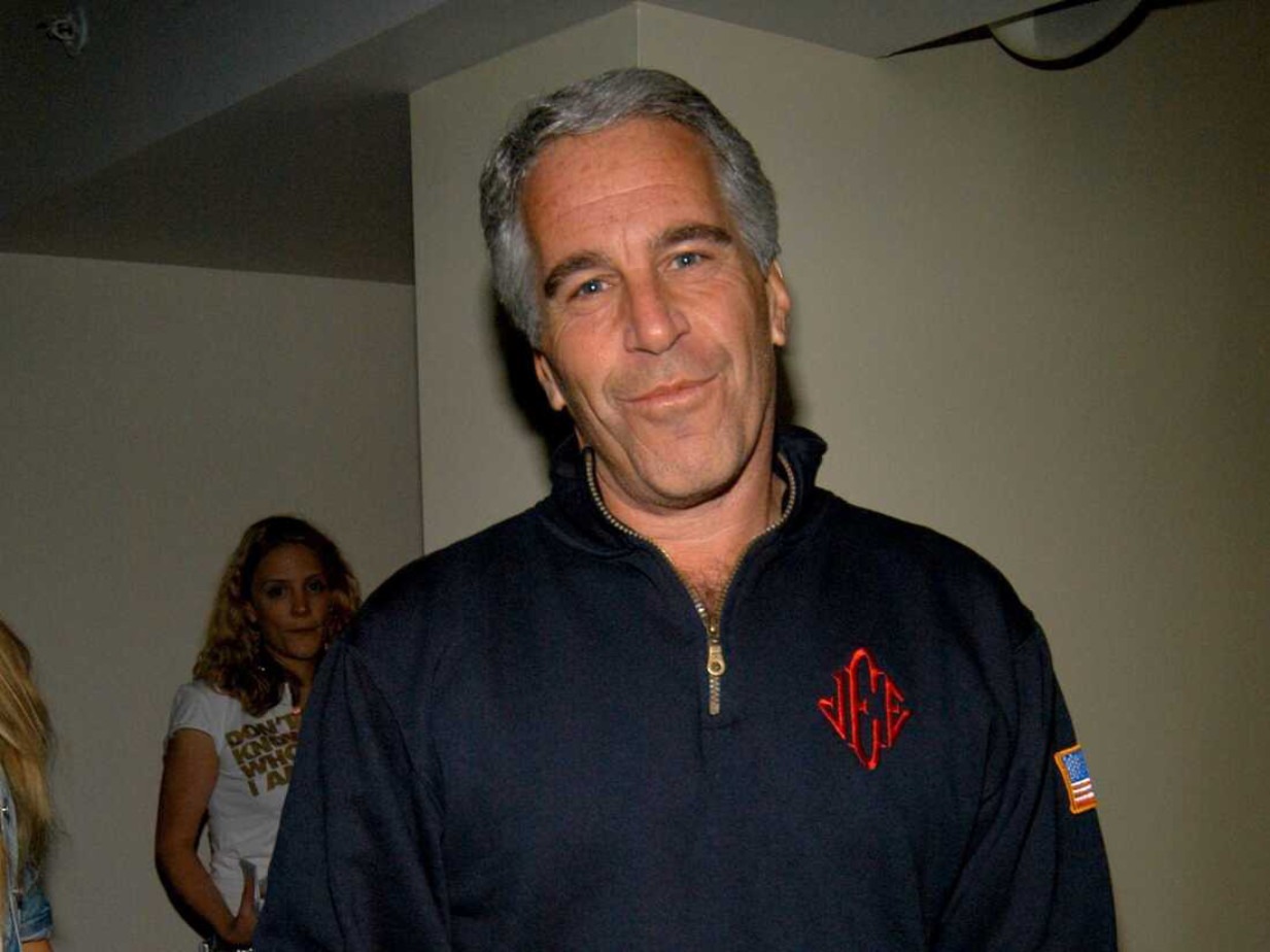 Man in dark zip-up sweater believed to be Jeffrey Epstein smirking at camera