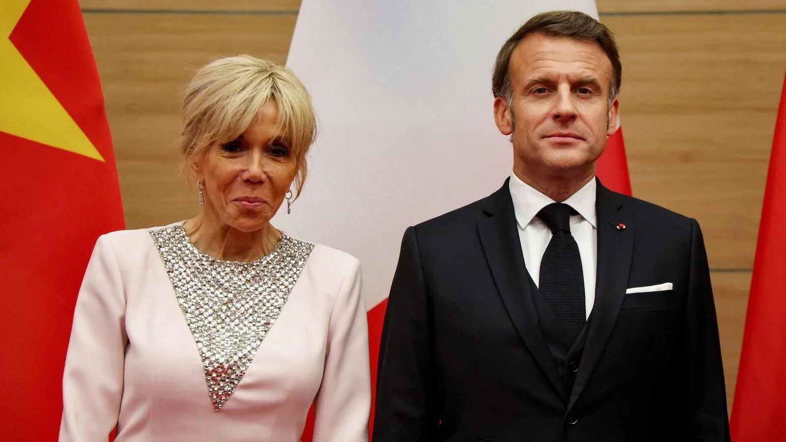 French President Emmanuel Macron and First Lady Brigitte Macron standing in front of flags