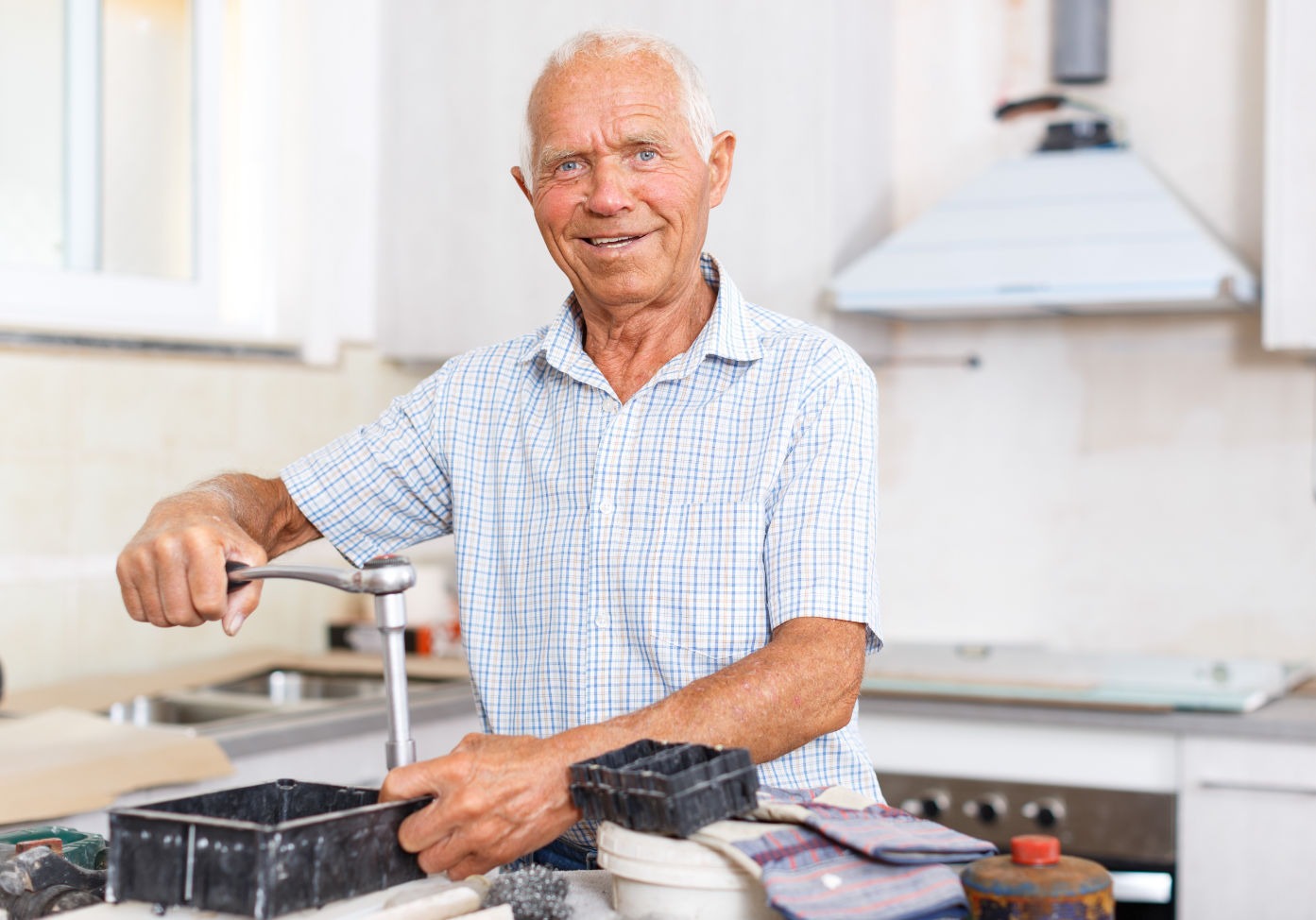 Retired man smiling while adjusting a working kitchen faucet with tools