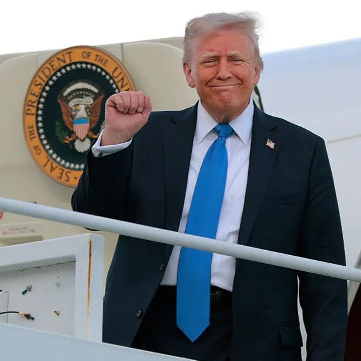 Donald Trump smiles and raises his fist while stepping off Air Force One
