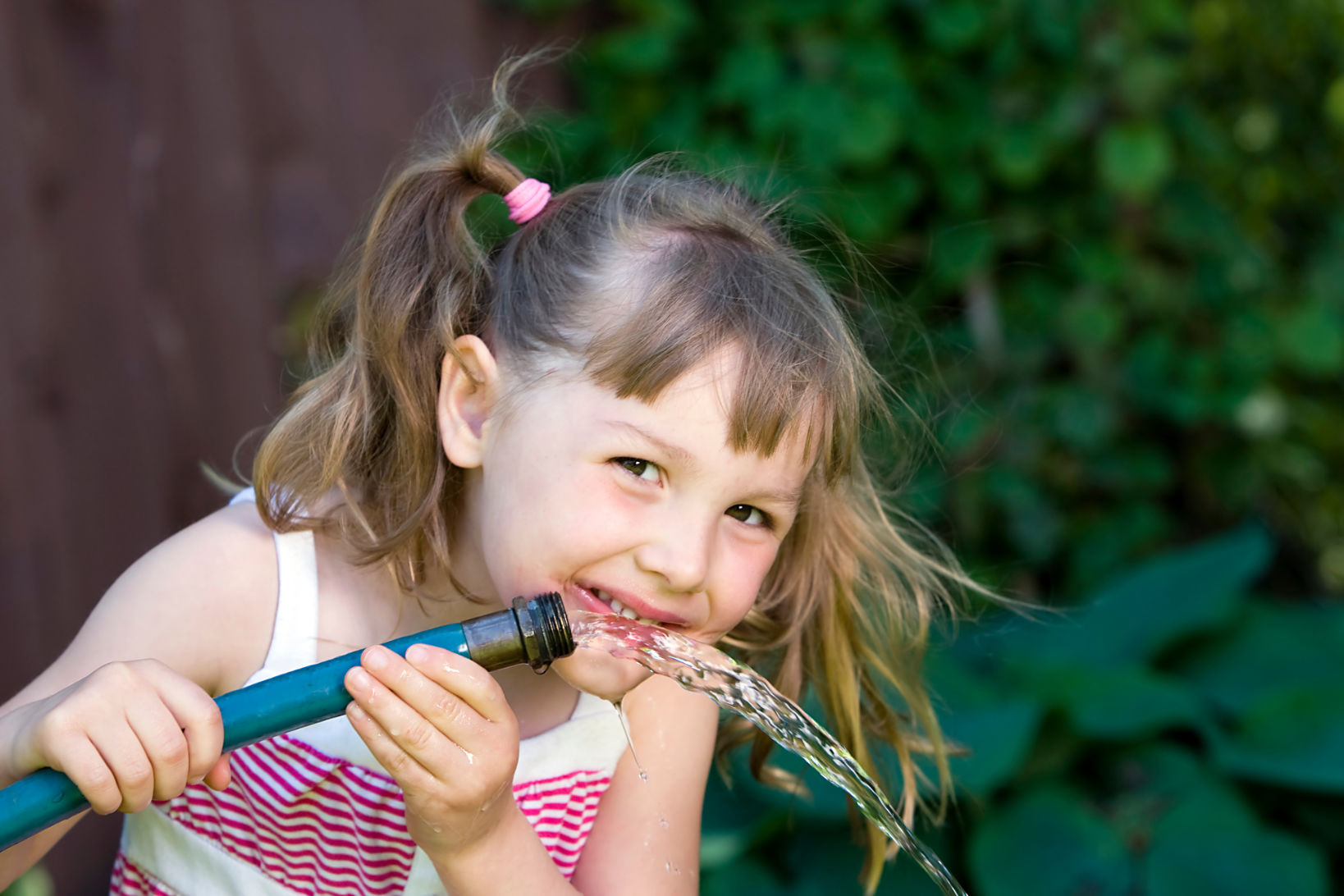 Child happily drinking water from a garden hose