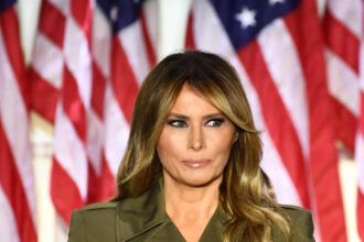 Melania Trump standing in front of American flags
