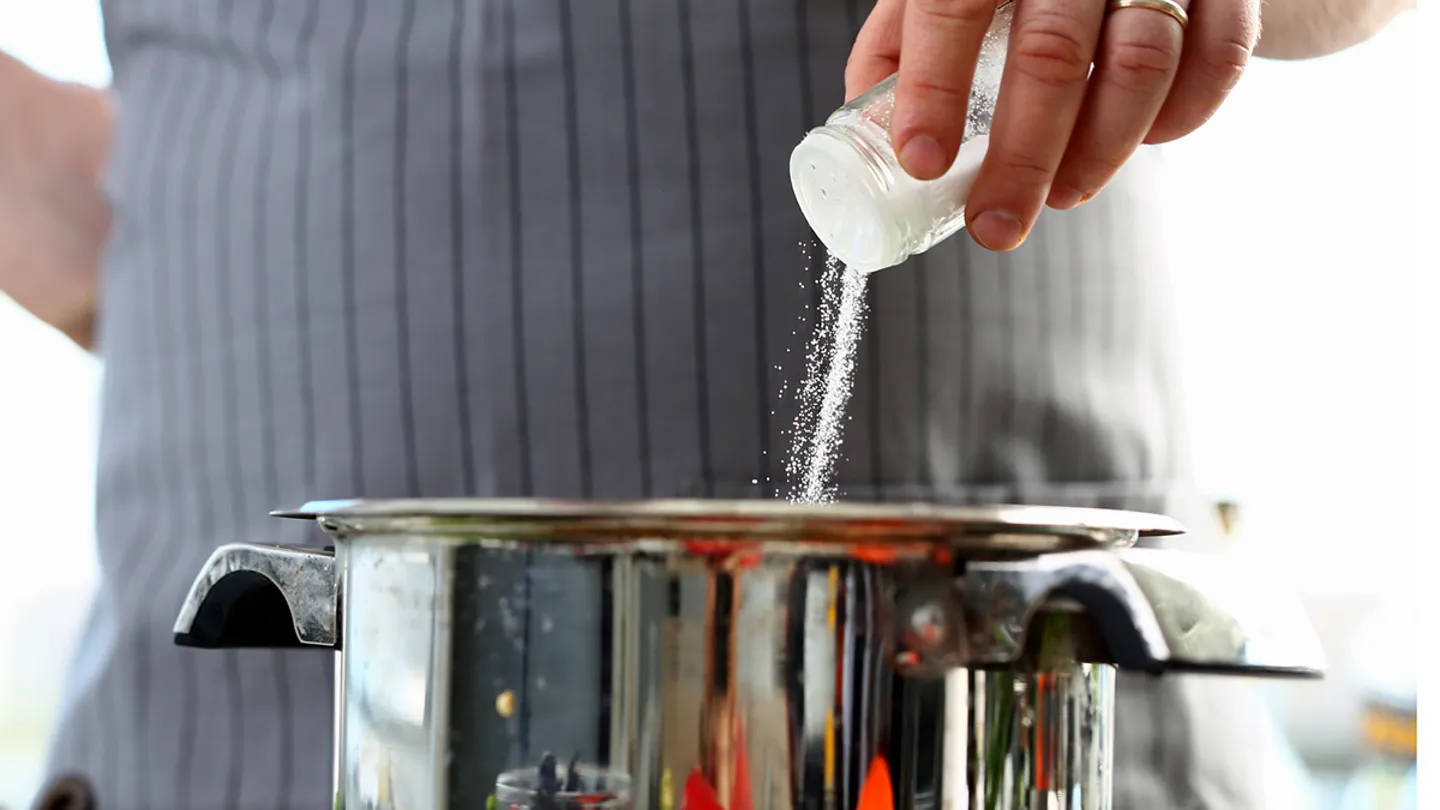 Close-up of person pouring salt into a pot on a stovetop.