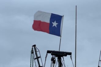 Texas state flag waving on a boat against cloudy sky.