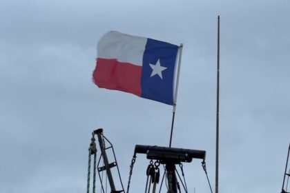 Texas state flag waving on a boat against cloudy sky.