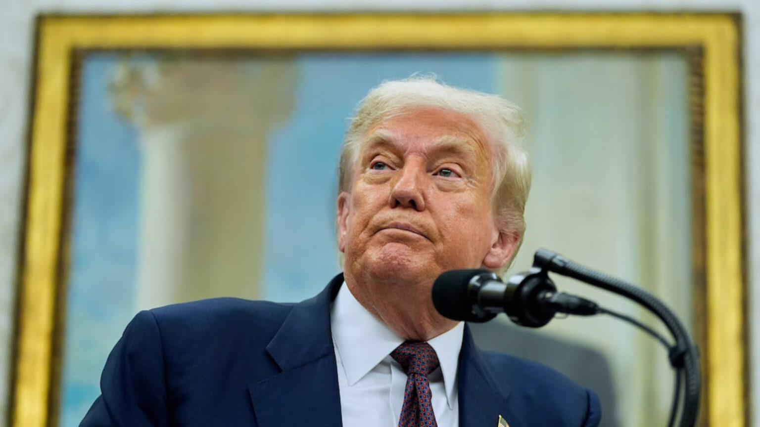 Donald Trump speaking at a podium with a painting in the background.