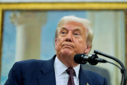 Donald Trump speaking at a podium with a painting in the background.