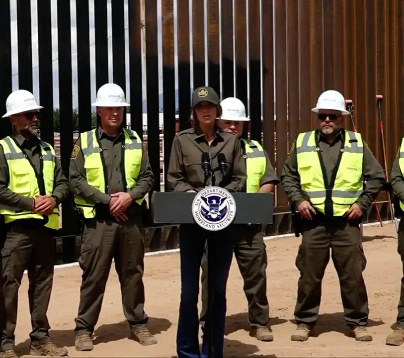 Homeland Security Secretary Kristi Noem speaks in front of border wall construction.