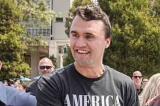 Charlie Kirk smiling at outdoor event surrounded by supporters