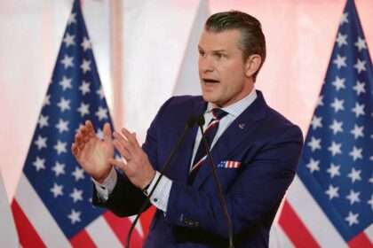 Pete Hegseth speaking before American flags at defense meeting