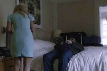 Rudy Giuliani reclines on a hotel bed with a woman standing nearby.