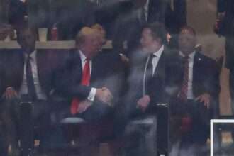 Donald Trump and Elon Musk shake hands while seated at an event.