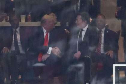 Donald Trump and Elon Musk shake hands while seated at an event.