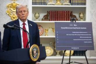 President Donald Trump stands next to a signboard announcing lower drug prices in the White House.