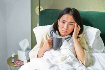 Woman sick in bed with cold holding a mug.