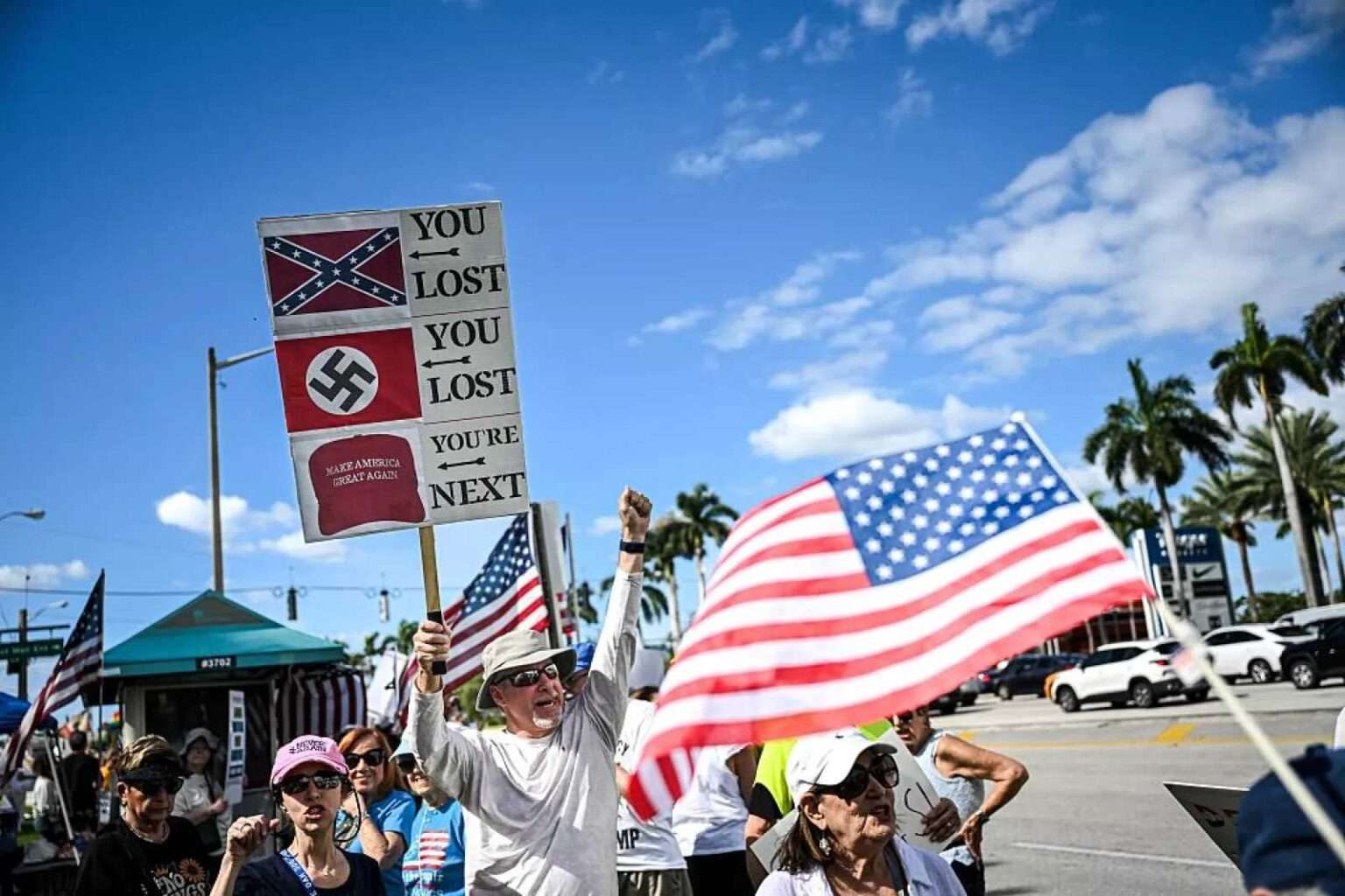 Protesters holding American flags and anti-authoritarian signs during a demonstration.