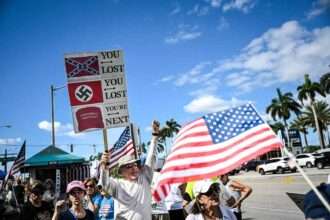 Protesters holding American flags and anti-authoritarian signs during a demonstration.