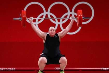 Olympic weightlifter performs a lift during competition with Olympic rings in background