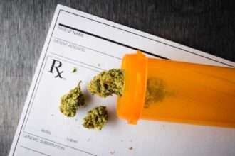 Dried cannabis buds spilling from an orange prescription bottle onto a medical prescription pad