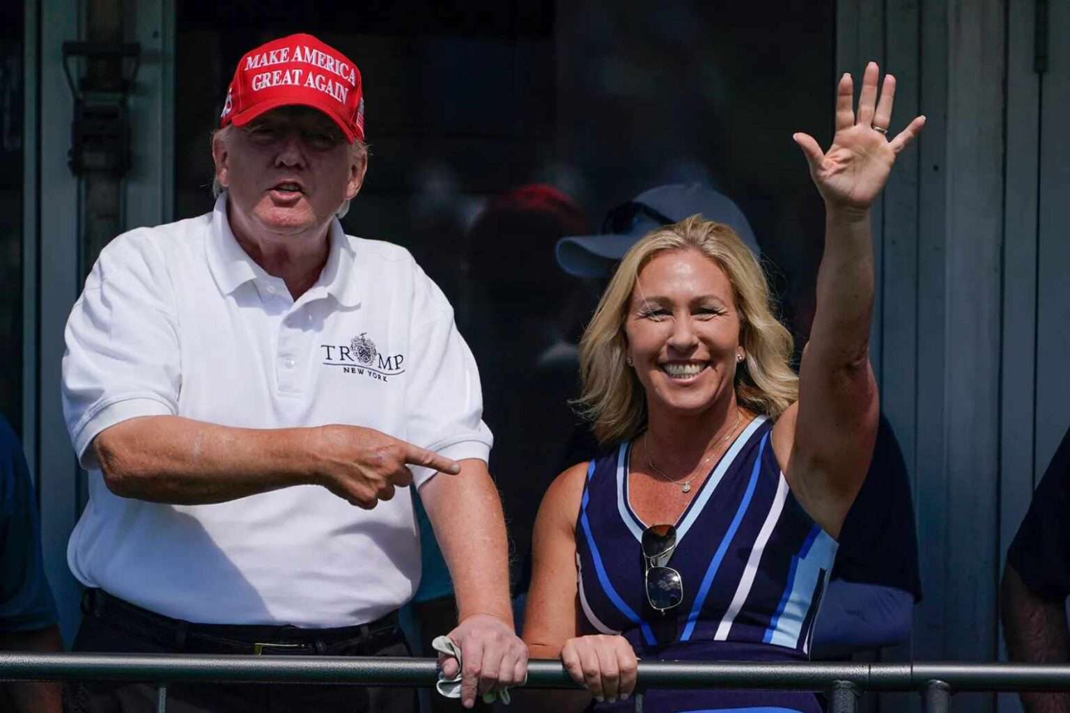 Donald Trump pointing while Marjorie Taylor Greene waves and smiles during an outdoor event.