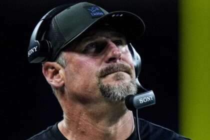 Detroit Lions head coach wearing a headset on the sideline during a game.