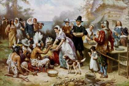 Historical painting showing Pilgrims and Native Americans sharing food at an outdoor feast during the first Thanksgiving.