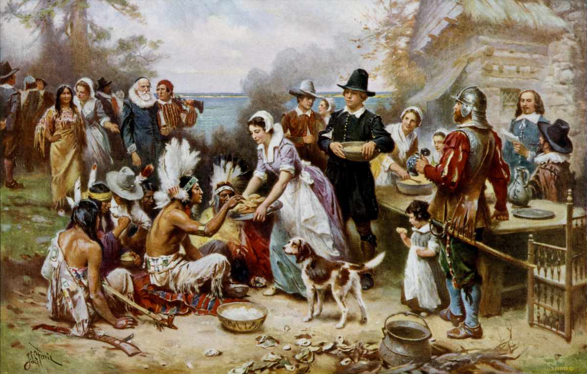 Historical painting showing Pilgrims and Native Americans sharing food at an outdoor feast during the first Thanksgiving.